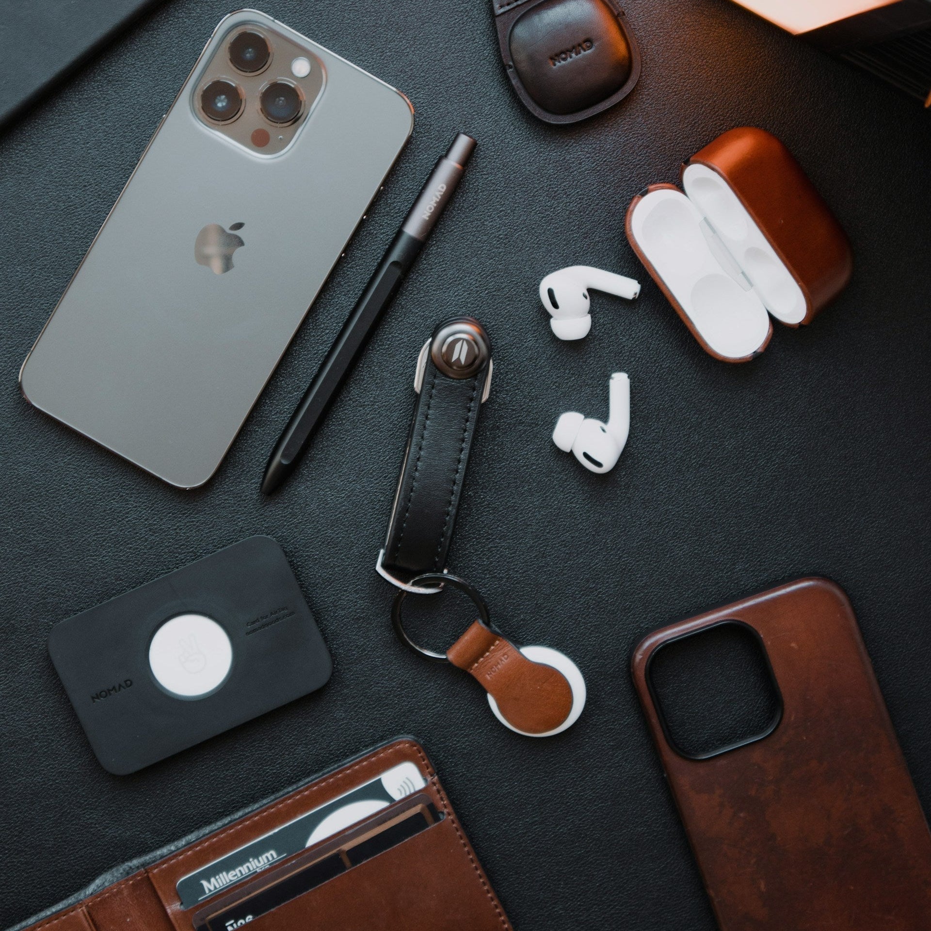 Collection of tech accessories including a phone, wallet, and earbuds on a dark surface.